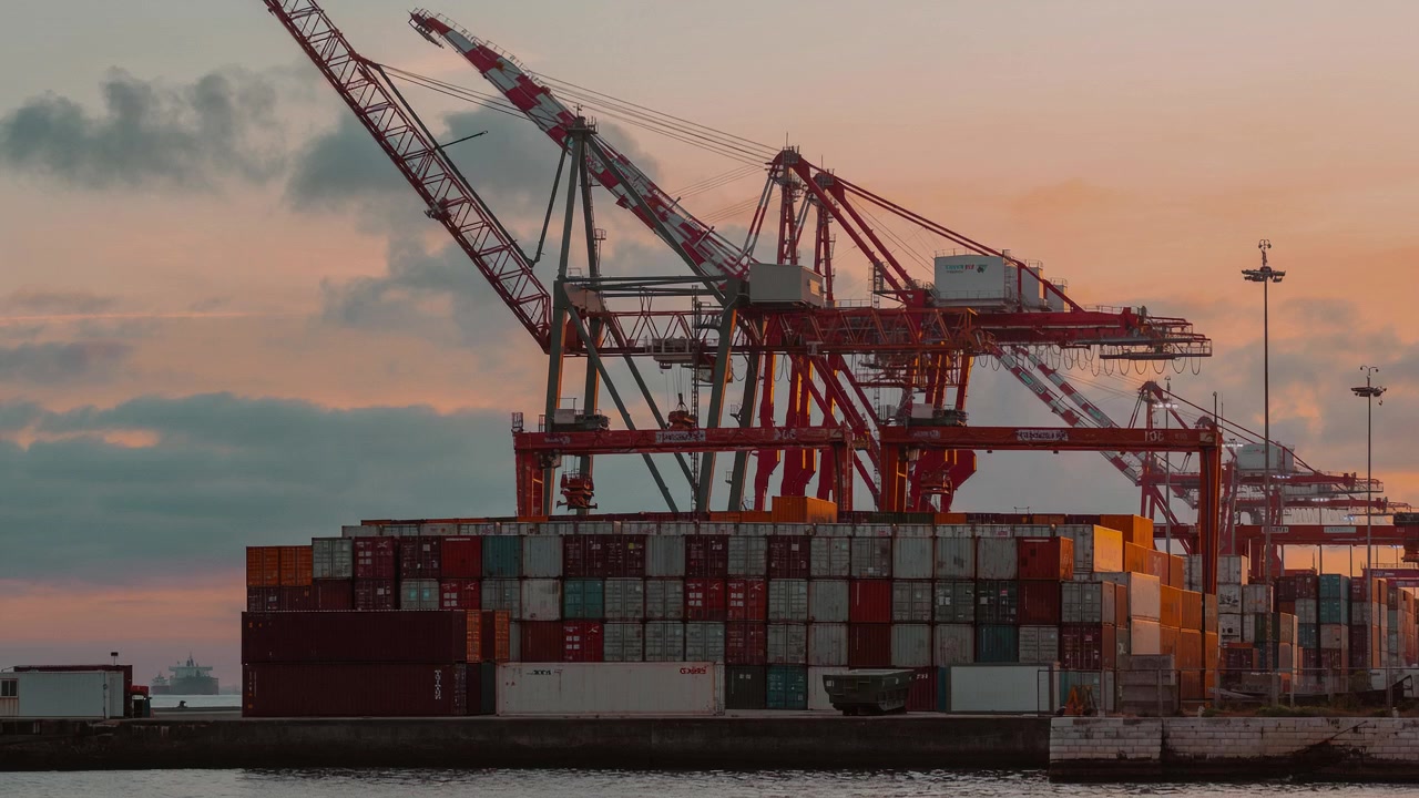 Shipping containers and port cranes at sunset.